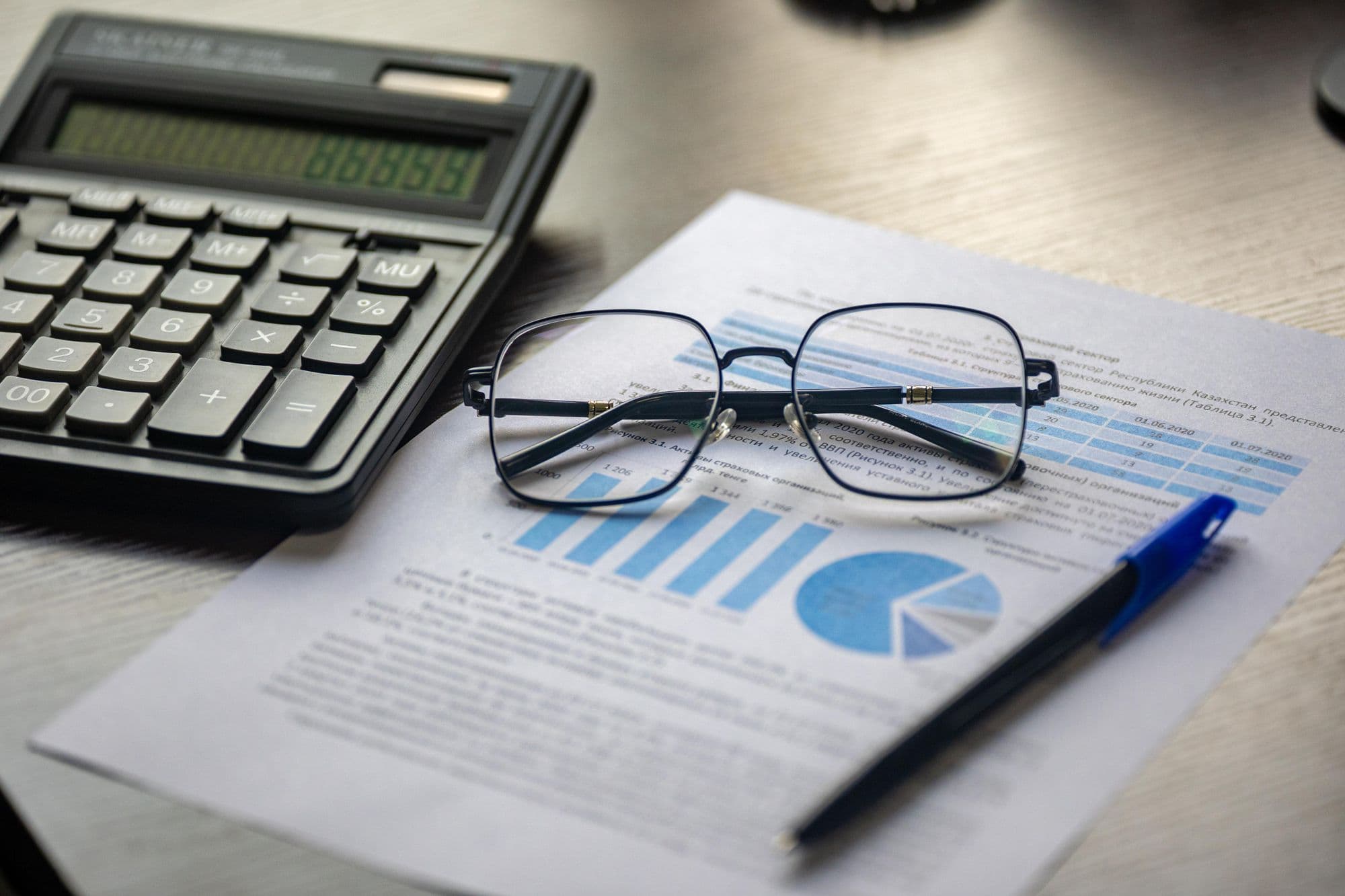 Un document financier, une calculatrice, un stylo et des lunettes sur un bureau.