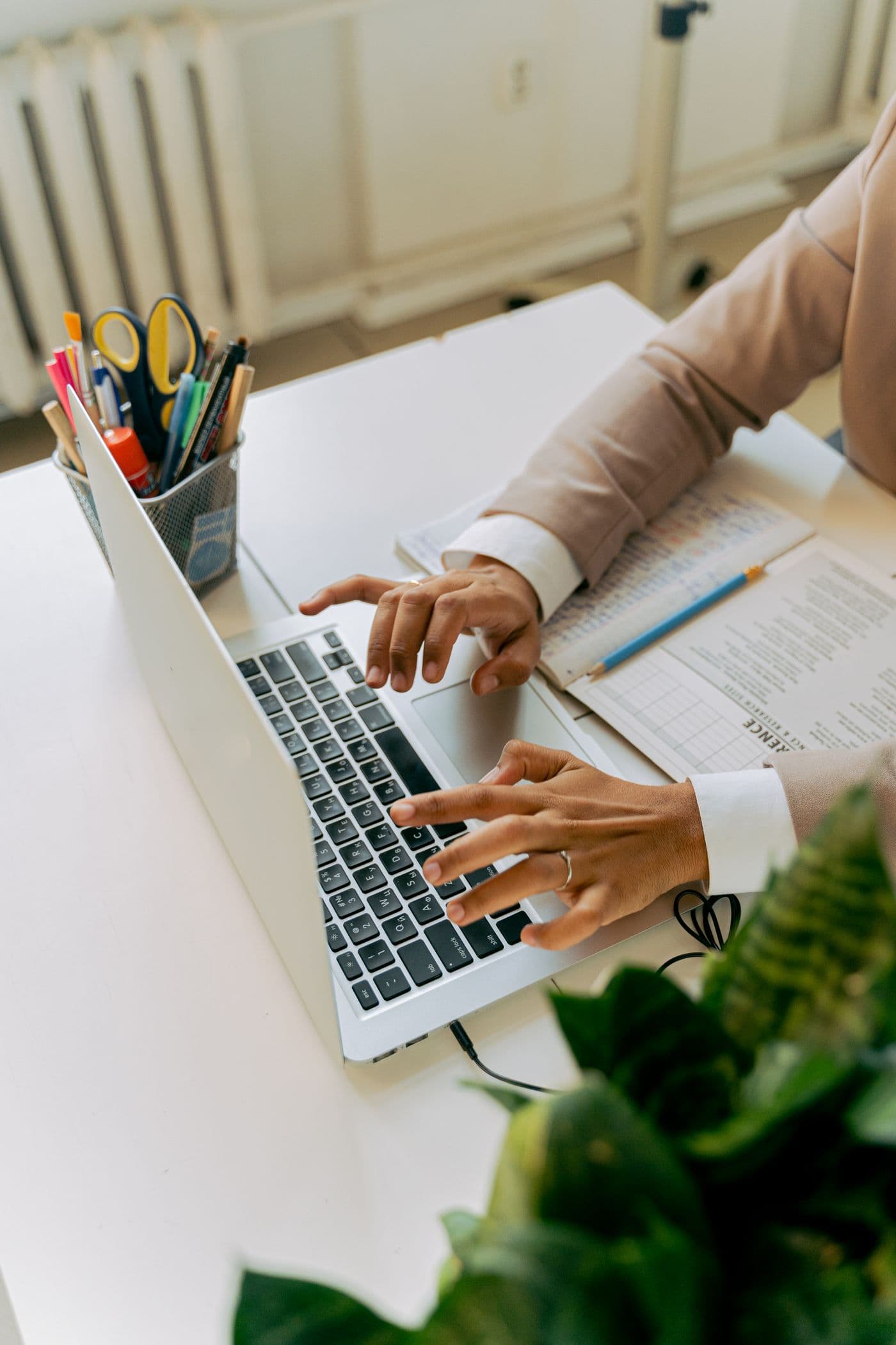 Une personne tape sur un ordinateur portable à un bureau bien rangé, entouré de plantes.