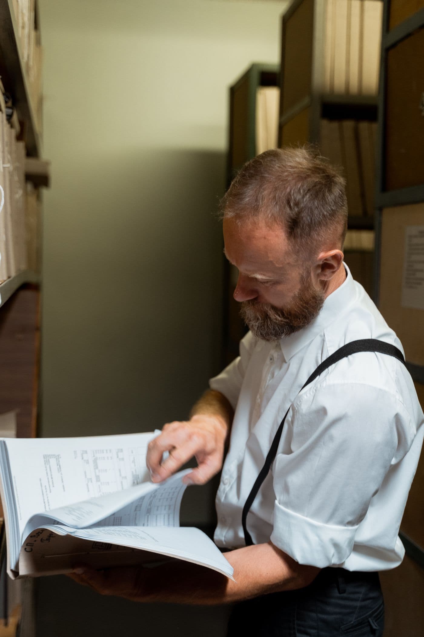 Un homme feuillette un grand registre dans les archives d’un bureau.
