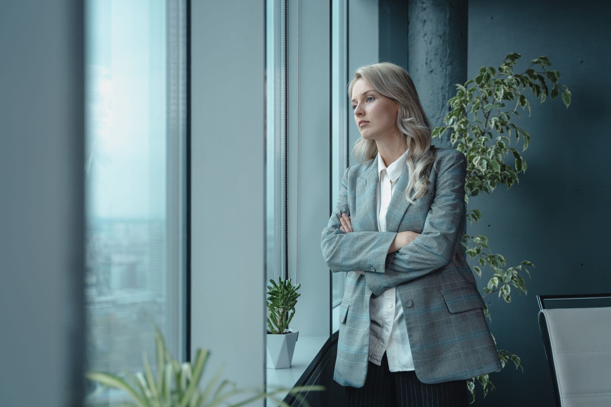 Une femme regarde pensivement par la grande fenêtre d’un bureau.
