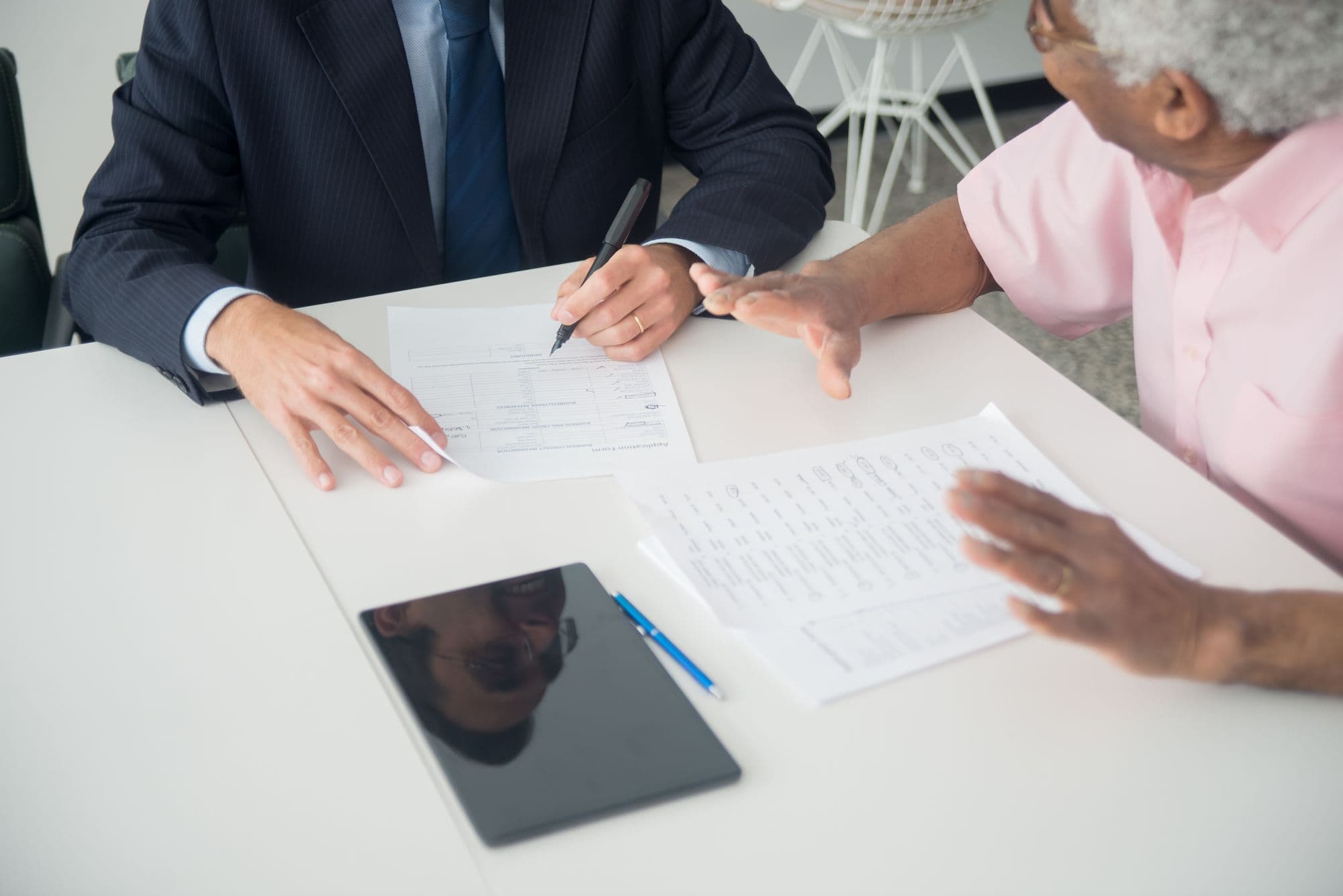 Un client âgé et un conseiller examinent des documents à une table de bureau.